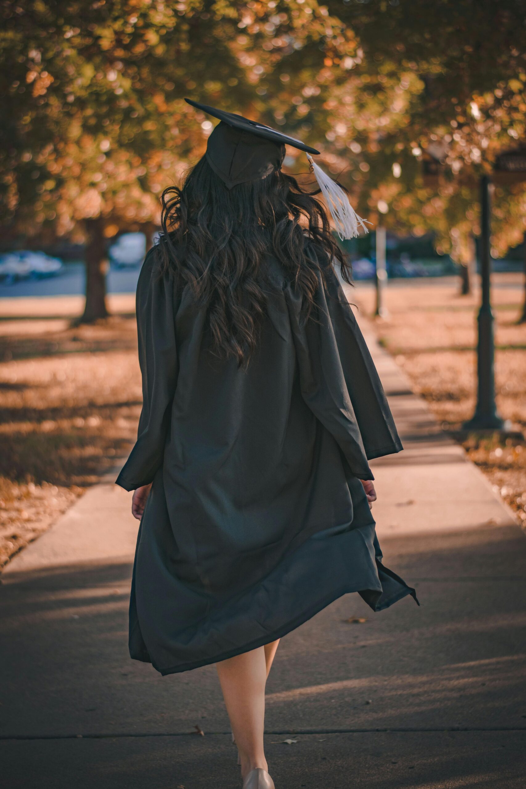 Back view of a graduate walking in an autumn park in academic dress.